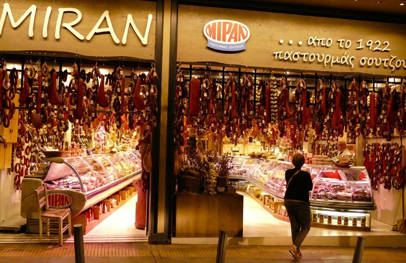 De buitenkant van een winkel, MIRAN, met hangend vlees. Iemand staat naar binnen te kijken.