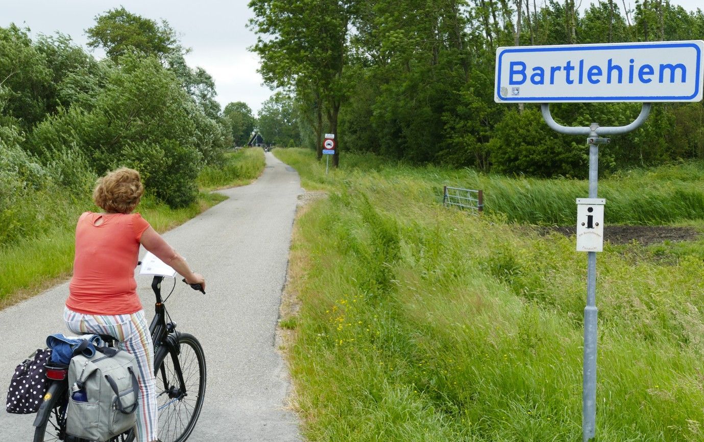 Een vrouw fietst op een verhard pad, omgeven door groen, richting een bord met 'Bartleheim'.
