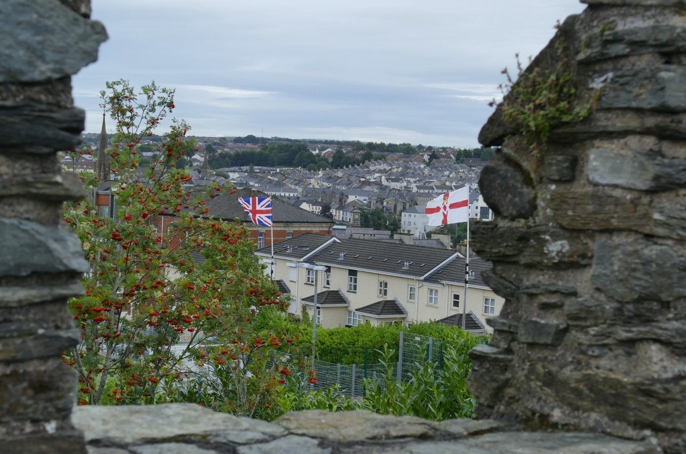 Uitzicht op een stad door een opening in een stenen muur, met Britse en Engelse vlaggen op de daken.