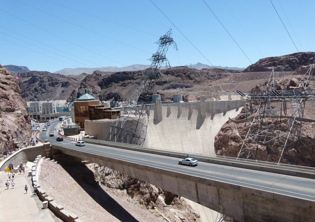 De Hooverdam met een weg, elektriciteitsleidingen en bergen op de achtergrond onder een heldere hemel.