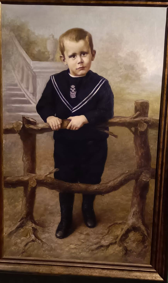 Een jong kind in een marine-uniform staat achter een rustieke houten schutting, in een geschilderd portret.