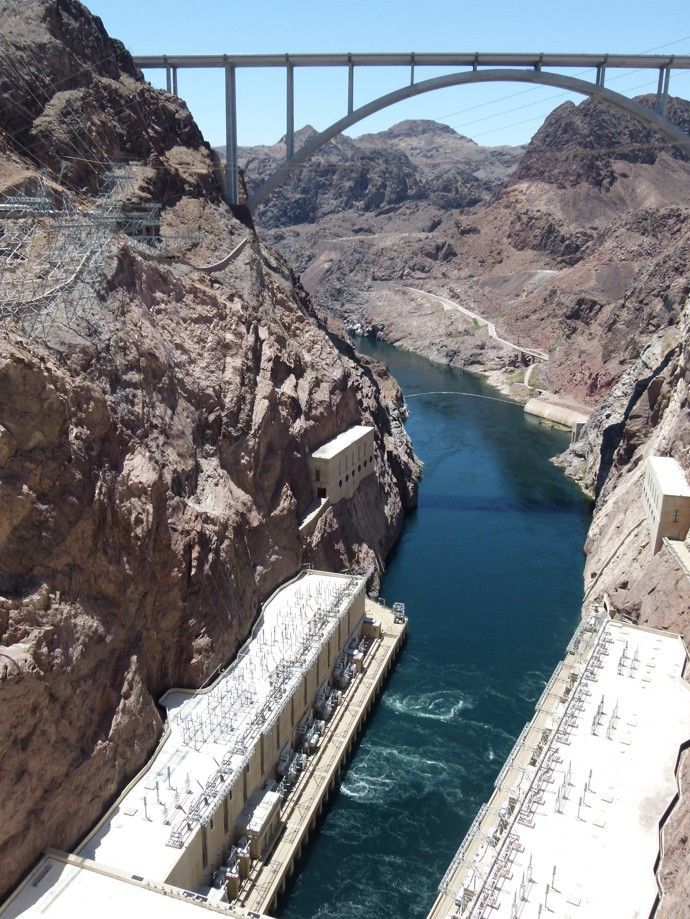 De Hooverdam en de brug over een turquoise rivier, geflankeerd door canyonwanden onder een blauwe hemel.