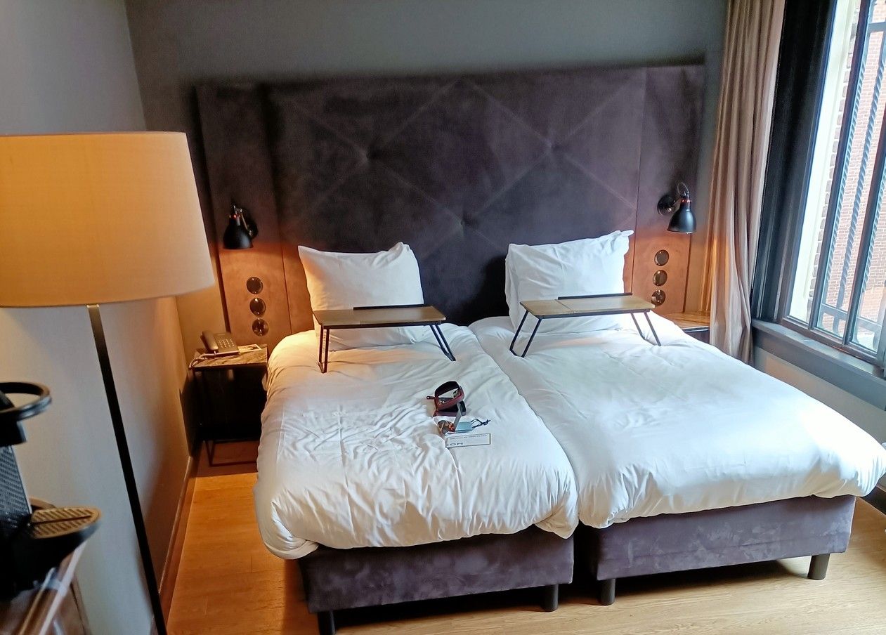 Slaapkamer met twee bedden, een groot hoofdeinde, nachtkastjes en kleine dienbladen.
