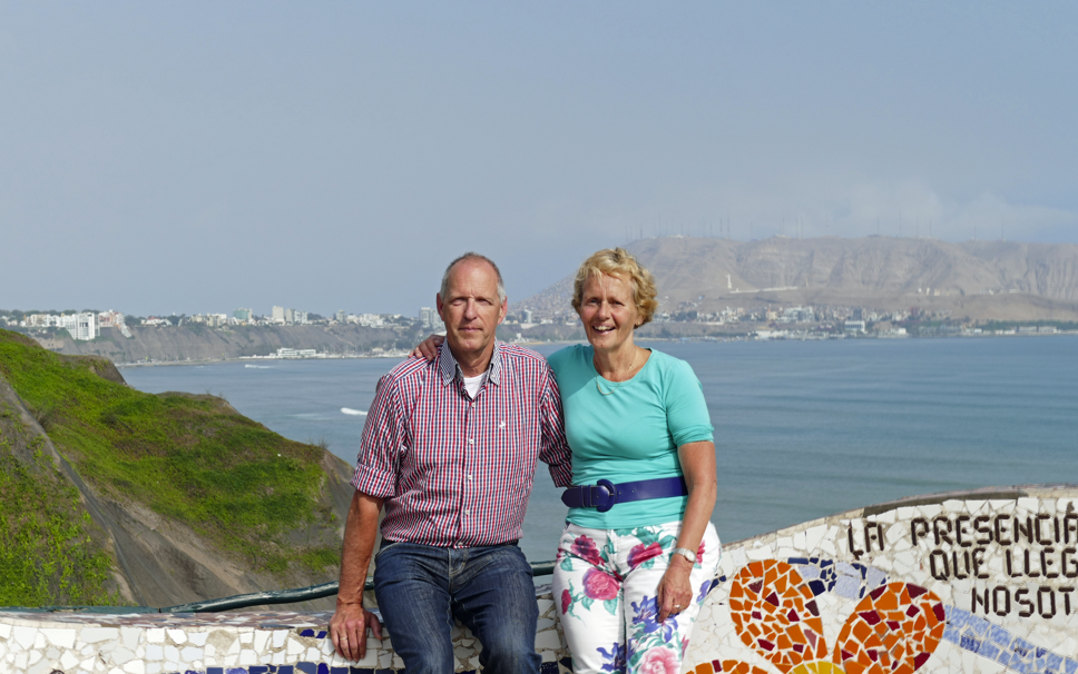Een stel poseert aan de kust, met de oceaan en de stad in het zicht, op een zonnige dag.
