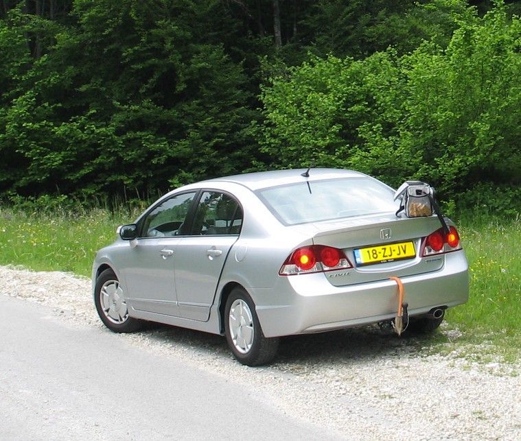 Een zilverkleurige Honda staat geparkeerd langs de weg, met een rugzak op de achterklep.  Locatie: Kroatië