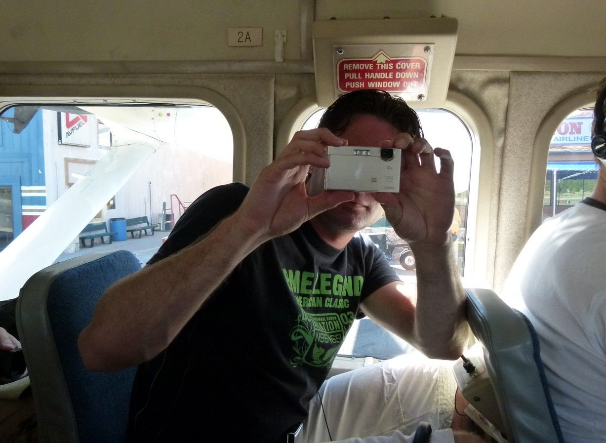 Een man in een zwart shirt maakt een foto met een kleine camera in een bus.