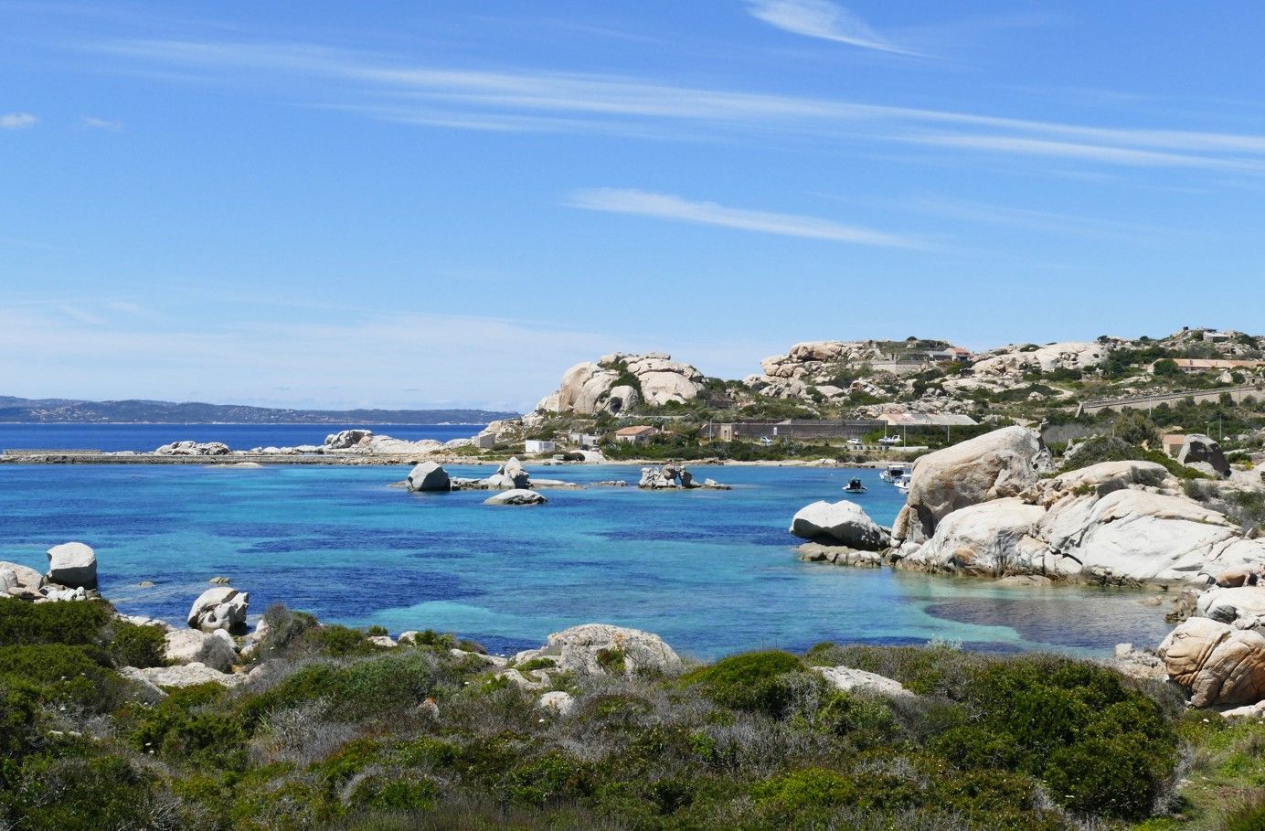 Schilderachtig uitzicht op een turquoise baai met grote granieten rotsformaties onder een helderblauwe hemel.