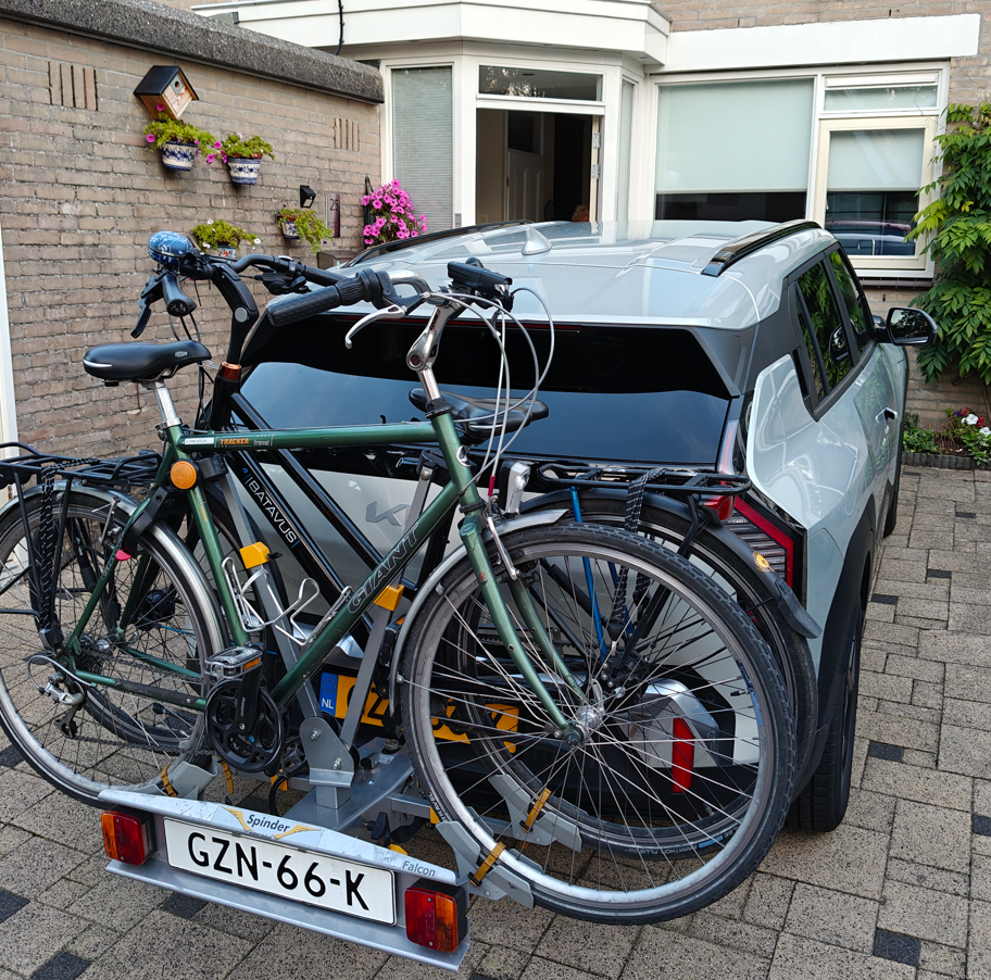 Twee fietsen gemonteerd op een auto die geparkeerd staat op de oprit bij een huis.