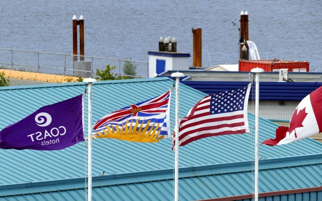 Vlaggen: Paarse kustvlag, Brits-Columbia, VS en Canada. Gebouw met schoorstenen en water op de achtergrond.