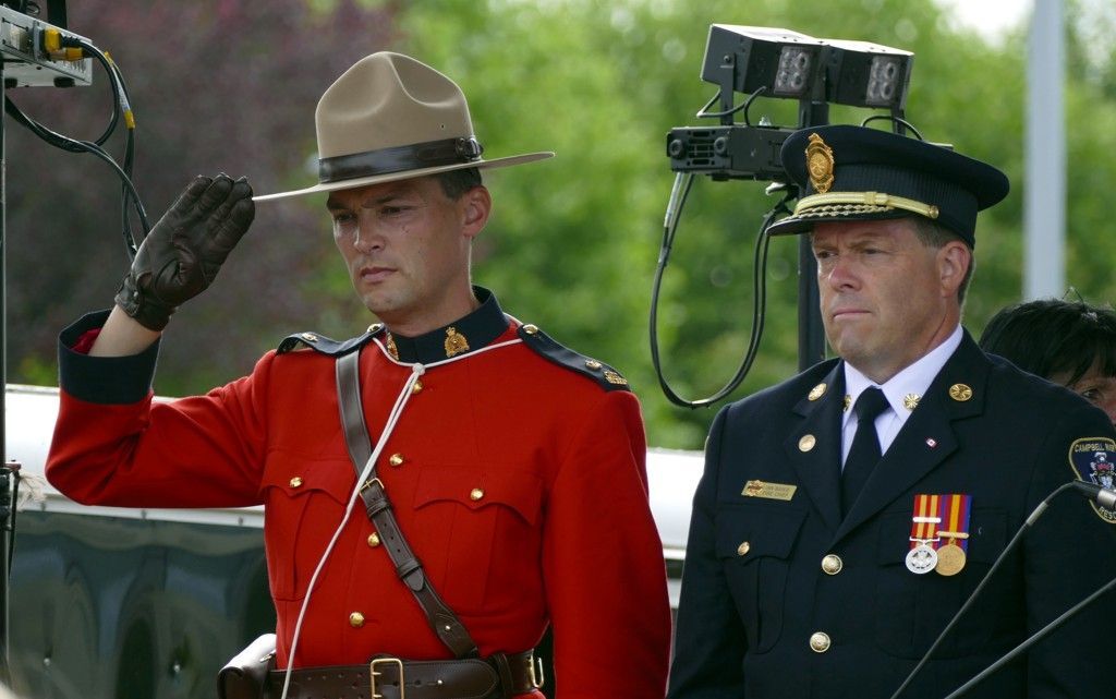 Een agent van de Royal Canadian Mounted Police in een rode jas brengt een saluut; een man in een marine-uniform staat naast hem.