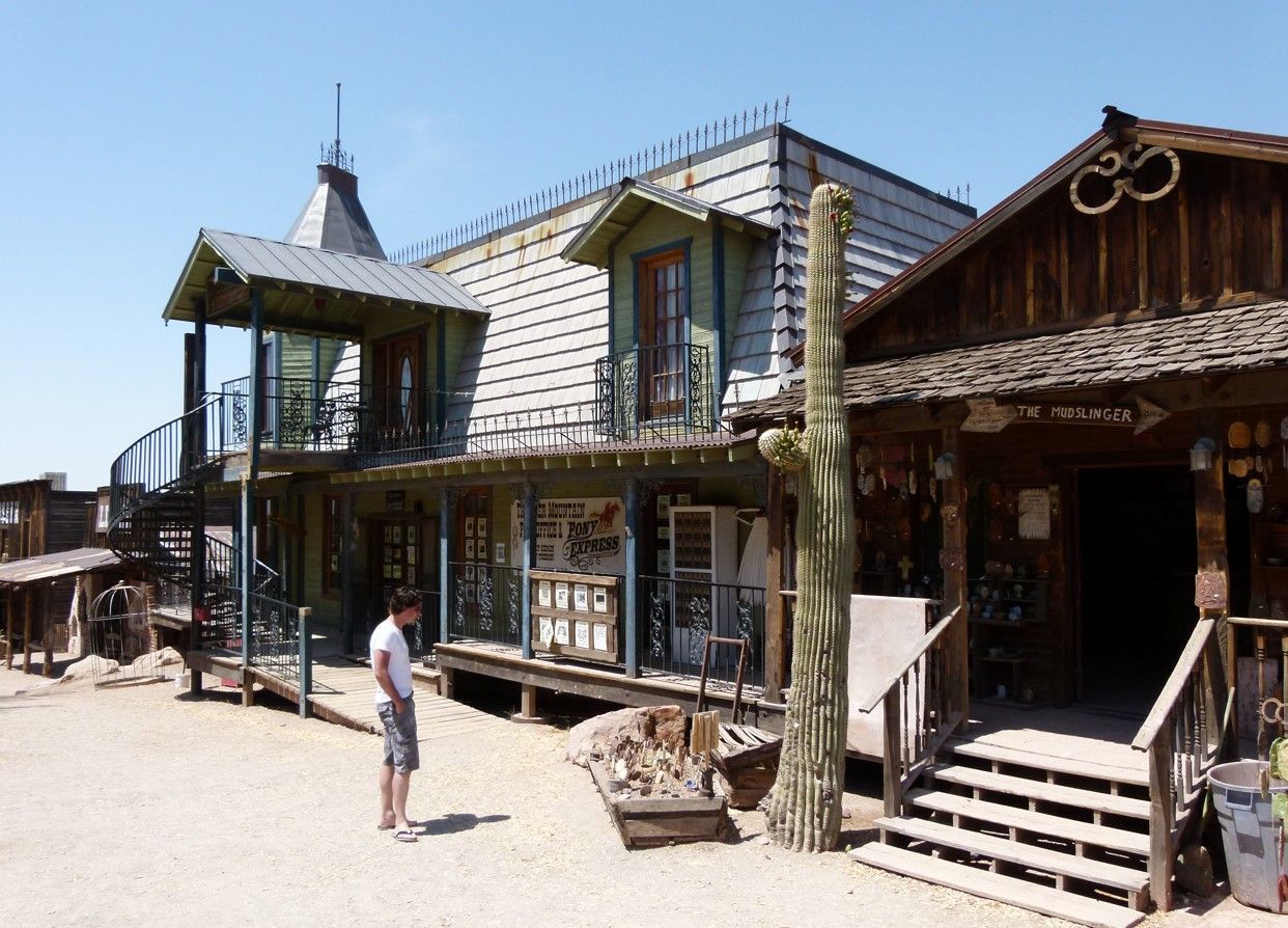 Oude gebouwen uit het Wilde Westen en een cactus onder een heldere hemel; een persoon staat op straat.