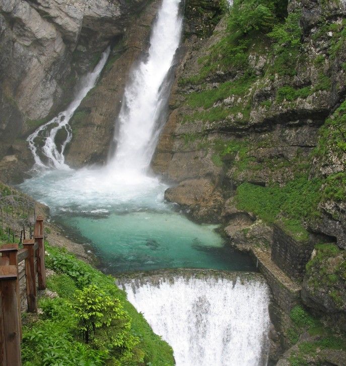 Een waterval die neerstort in een turquoise poel, omgeven door rotswanden en groene vegetatie.