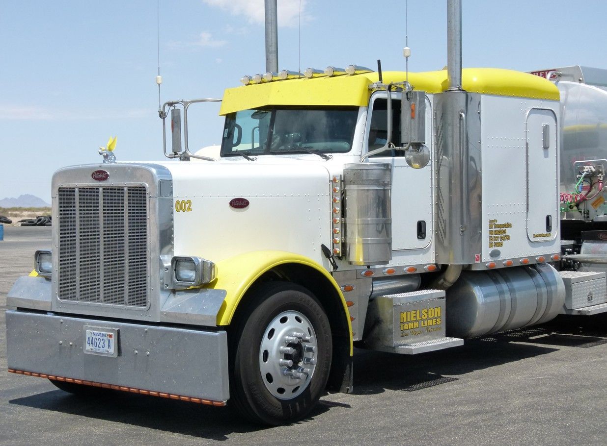 Een witte en gele Peterbilt-vrachtwagen staat buiten geparkeerd op het asfalt, op een zonnige dag.