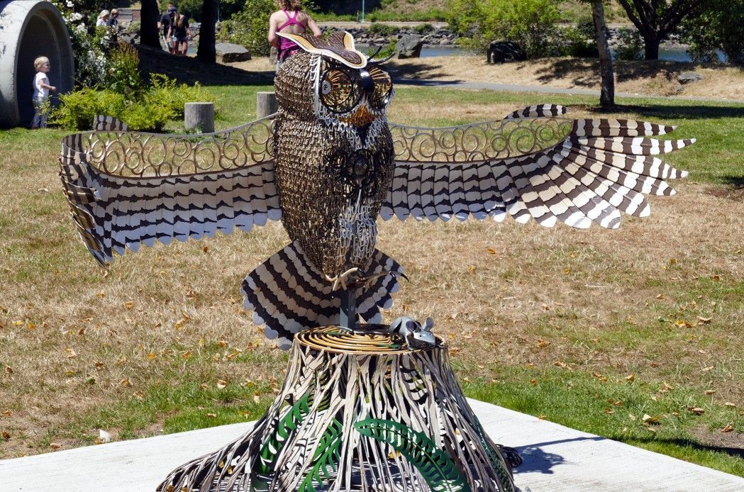 Een uilensculptuur met uitgestrekte vleugels op een boomstronk, in een park.