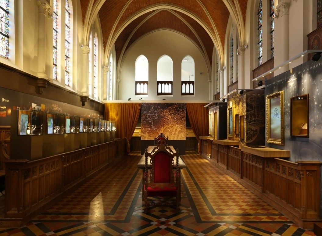 Grote ceremoniezaal met gewelfd plafond, houten lambrisering, kroonluchters en een centrale rode troonachtige stoel.