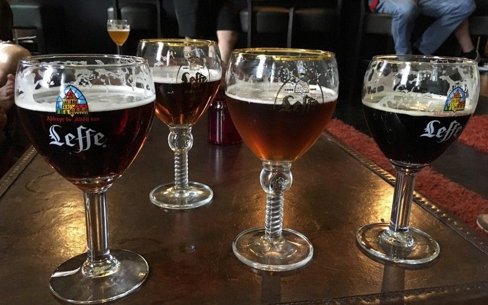 Vier Leffe-bierglazen op een houten tafel in een schemerig verlichte bar.
