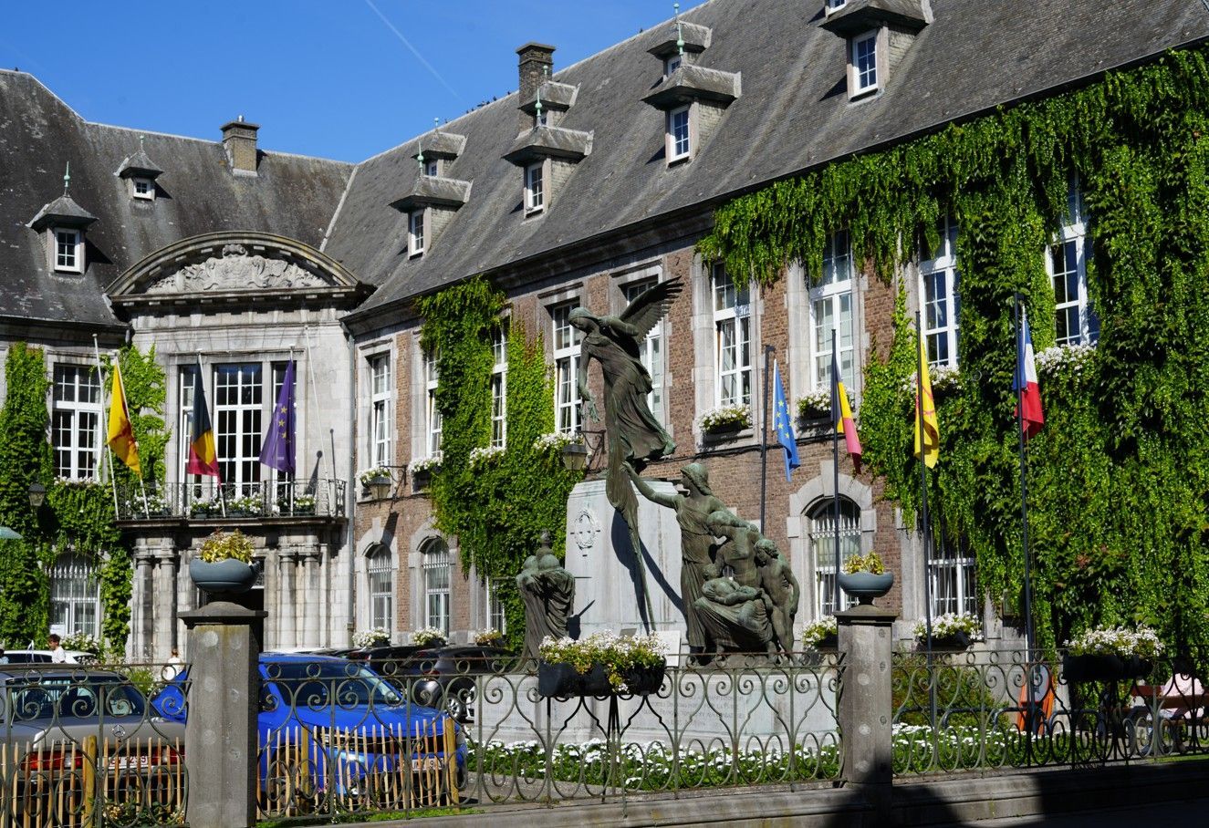 Historisch stenen gebouw met klimop, stenen daken en een centraal standbeeld in een binnentuin.