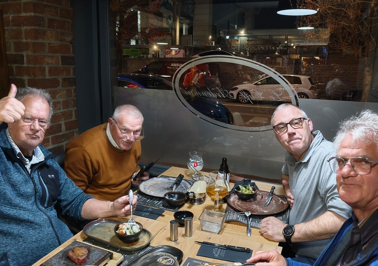 Vier personen zitten aan een restauranttafel te eten, waarbij één persoon een duim omhoog steekt.