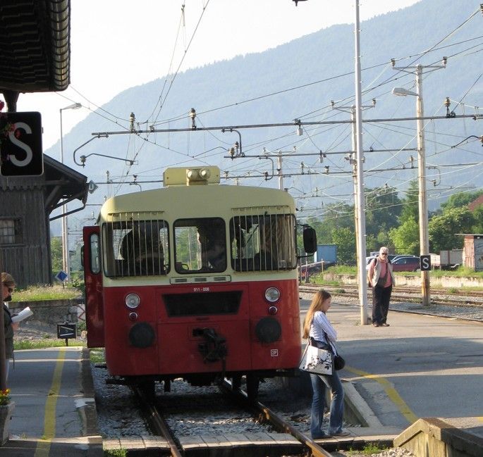 Een rood-crèmekleurige trein staat op een station. Een vrouw stapt uit. Een man staat er vlakbij. 