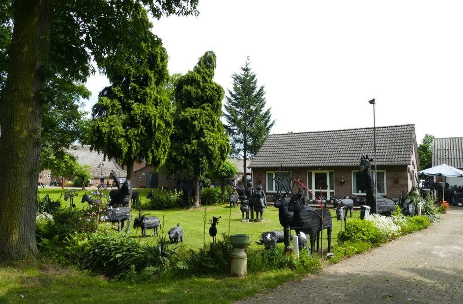 Een tuin vol metalen dierensculpturen voor een bakstenen gebouw en bomen.