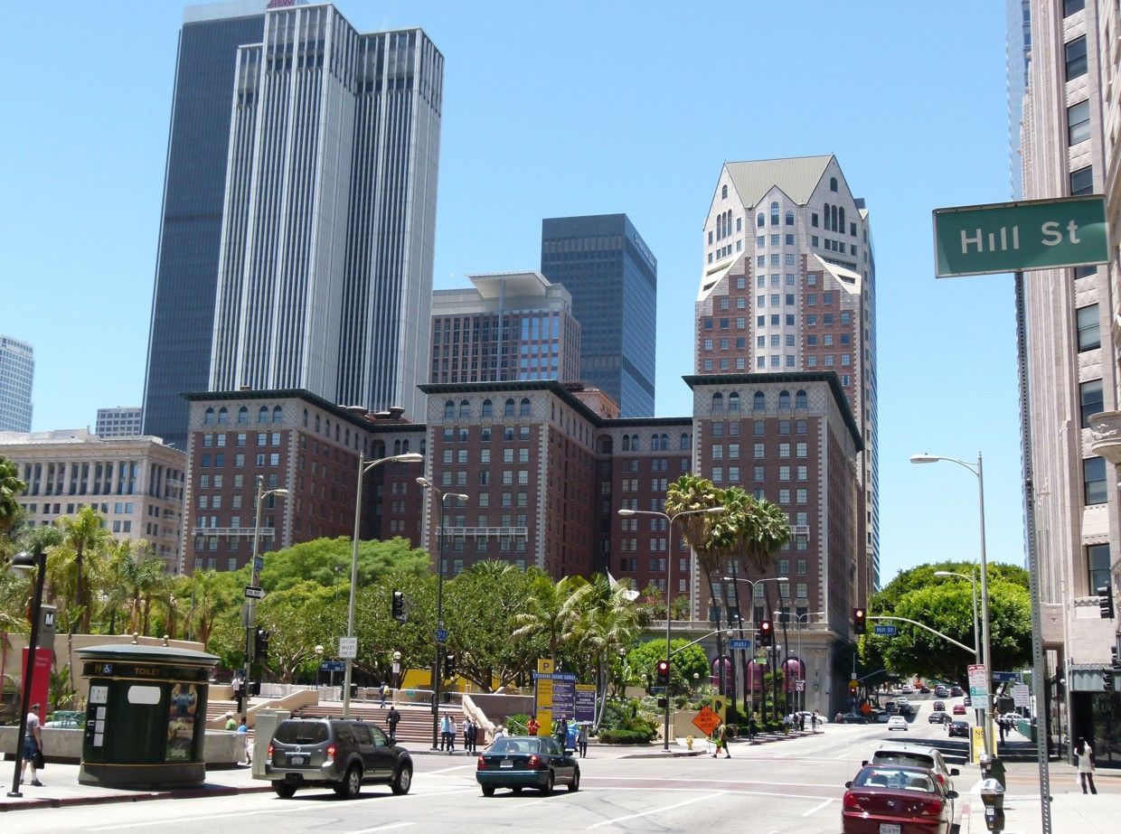 Stadsgezicht van het centrum van Los Angeles met auto's op straat, gebouwen, palmbomen en een straatnaambord.