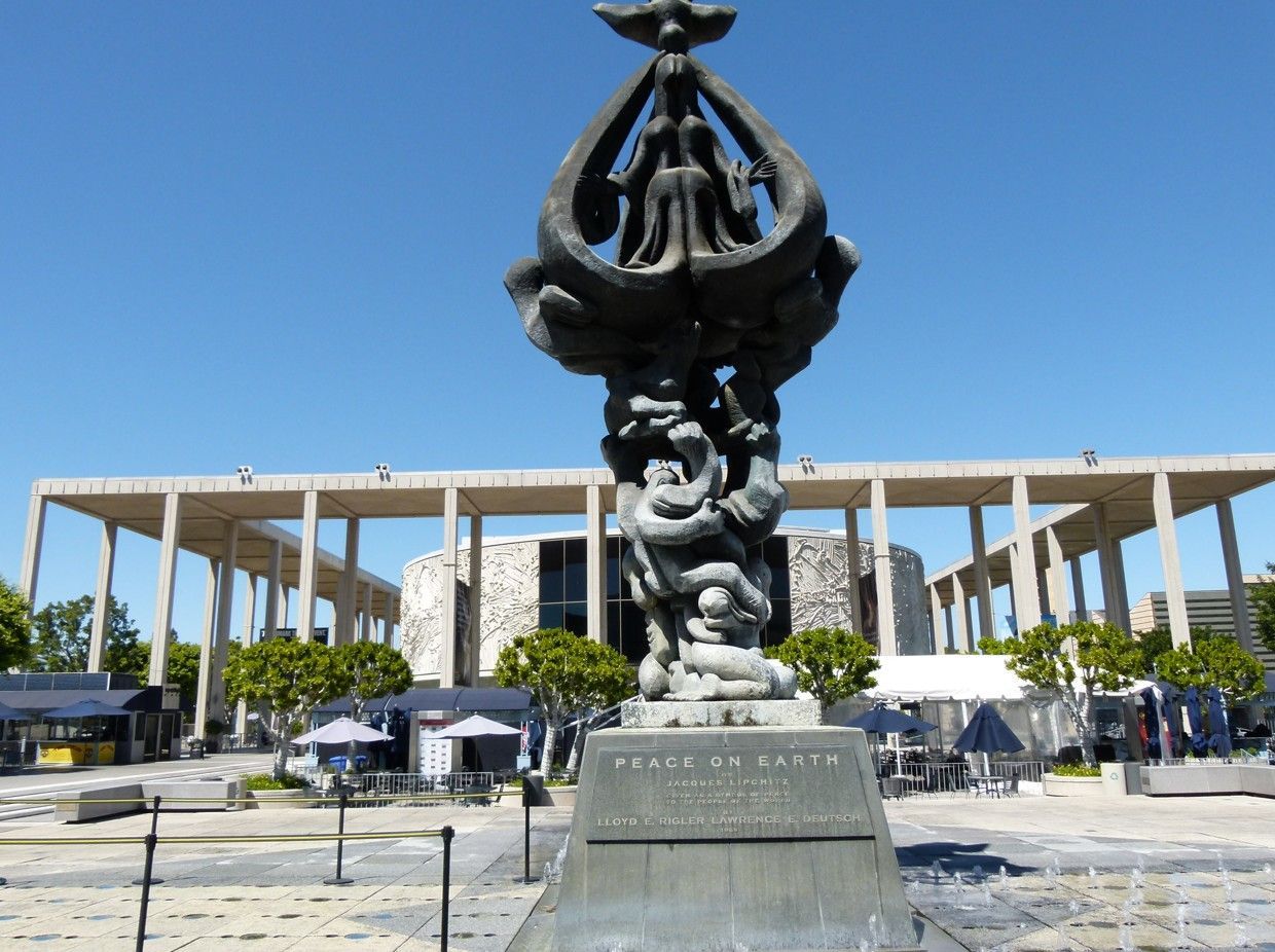 Een sculptuur voor een modern gebouw; mensen, bronzen figuren, een duif, alles onder een blauwe hemel.