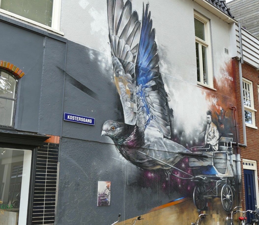 Muurschildering van een grote vogel met gespreide vleugels die een koets trekt. Kleuren: grijs, blauw en wit. 