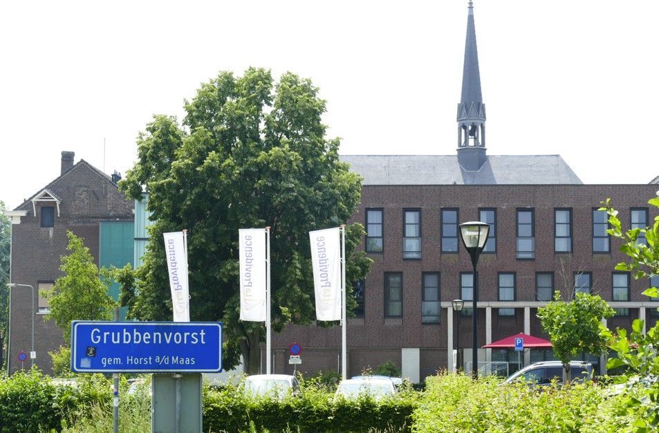 Het bord naar Grubbenvorst, met op de achtergrond een gebouw en een torenspits, is op een zonnige dag goed zichtbaar.