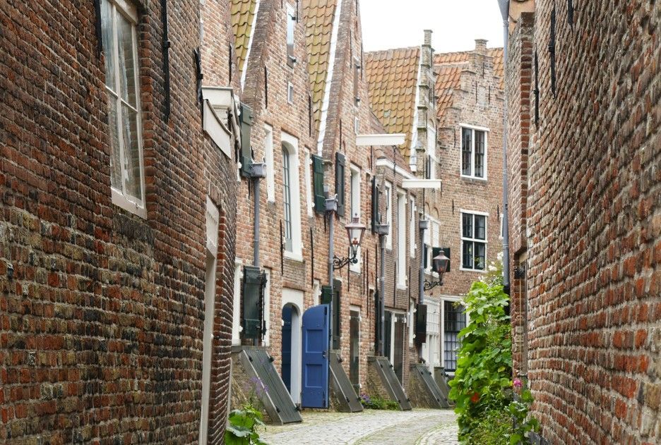 Smalle bakstenen steeg met gebouwen met puntgevels en een blauwe deur.