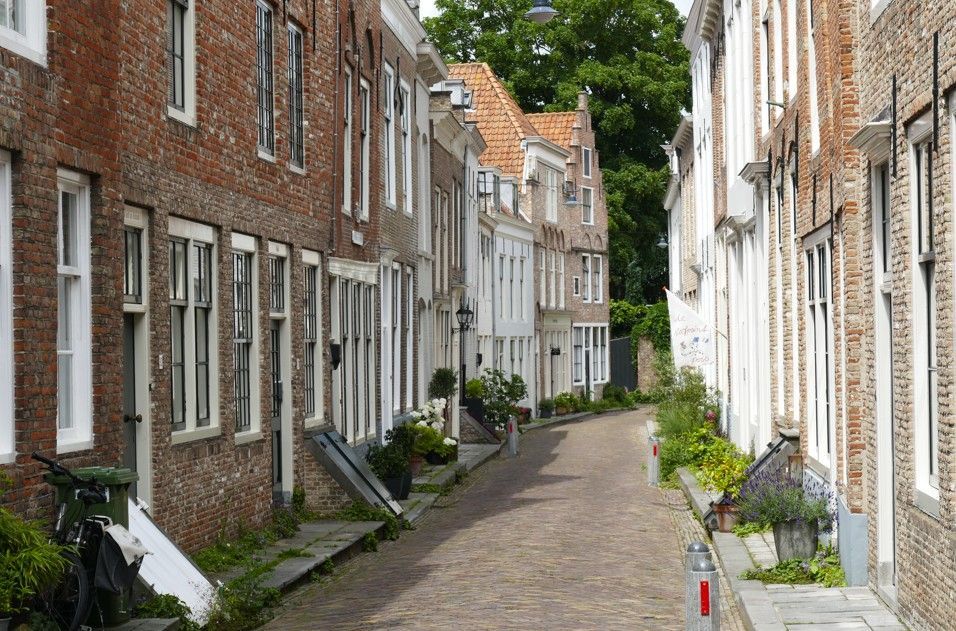 Smalle straat met bakstenen en witte gebouwen; een fiets leunt tegen een bakstenen gebouw aan de linkerkant.
