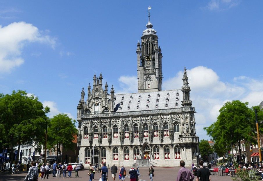 Stadhuis in gotische stijl met een hoge toren, mensen ervoor, blauwe lucht.
