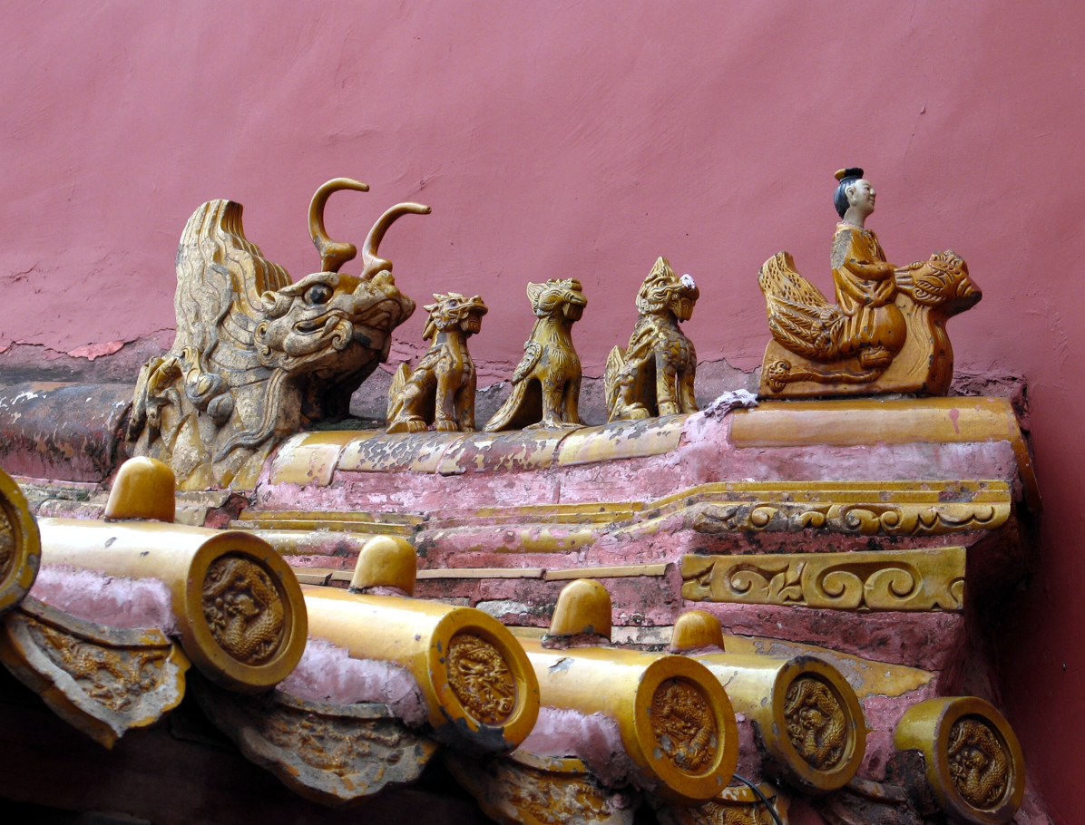 Een sierlijk keramisch dak met dierenfiguren tegen een roze muur.