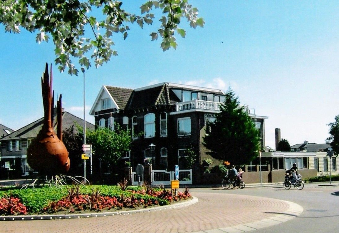 Rotonde met sculptuur en gebouw, fietsers en blauwe lucht.