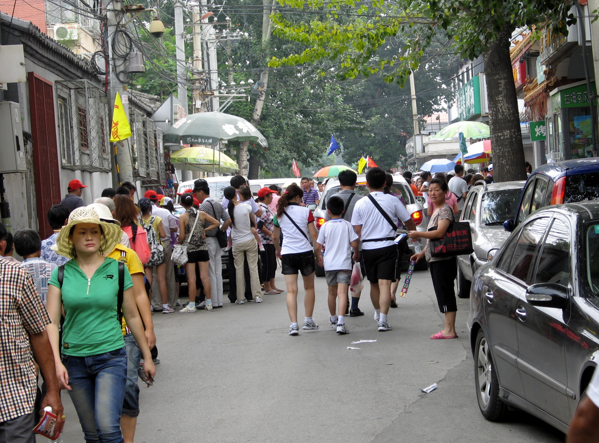 Een straatbeeld in China vol voetgangers en geparkeerde auto's.