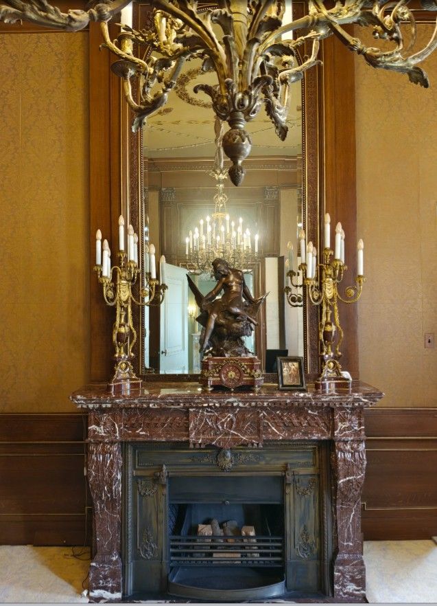 Een kamer met een open haard, een marmeren schoorsteenmantel, een spiegel en een bronzen sculptuur.