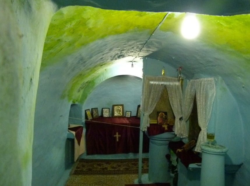 Interieur van een kleine, gewelfde, blauwgeschilderde grotkapel met een rood gedrapeerd altaar en religieuze iconen.