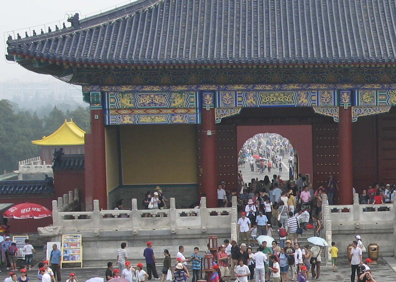 Ingang van een Chinese tempel met mensen. Rood en blauw gebouw met een sierlijk dak. Menigte stroomt naar binnen.