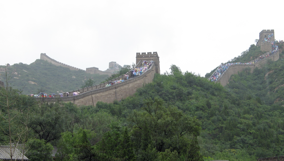 De Grote Muur van China slingert zich door een weelderig groene berg, met vele mensen die eroverheen lopen.