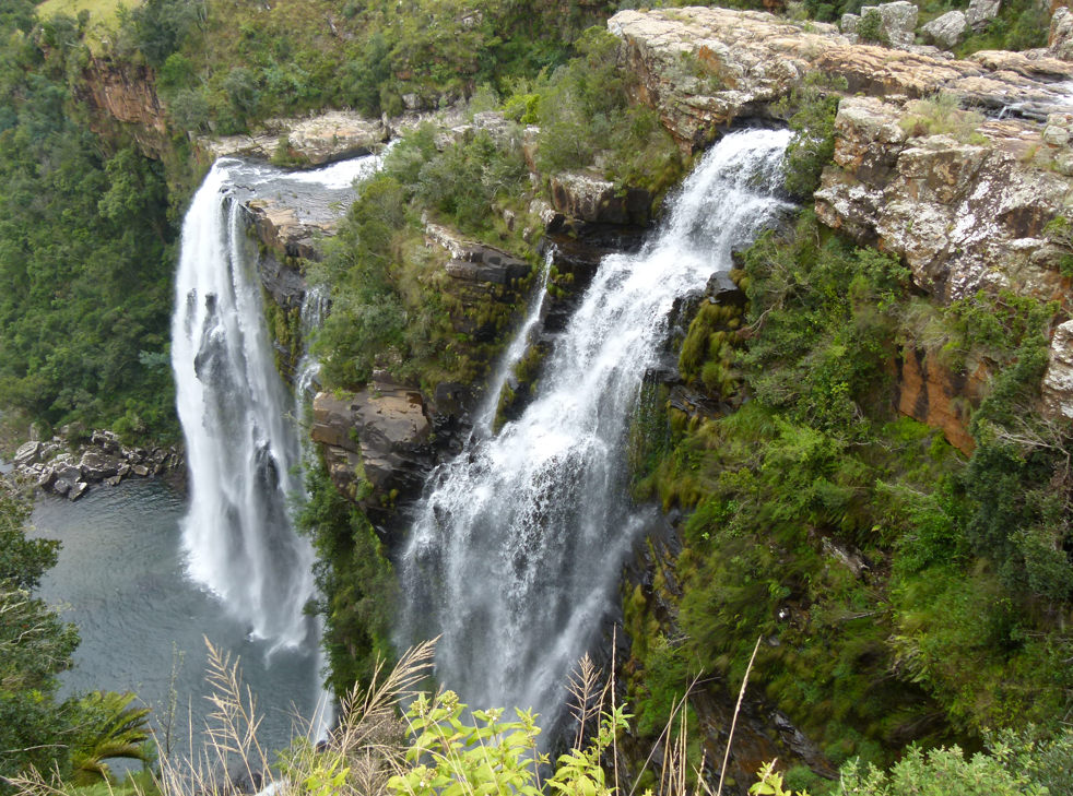 Een waterval die over rotsachtige kliffen naar beneden stort, omgeven door weelderige groene vegetatie.