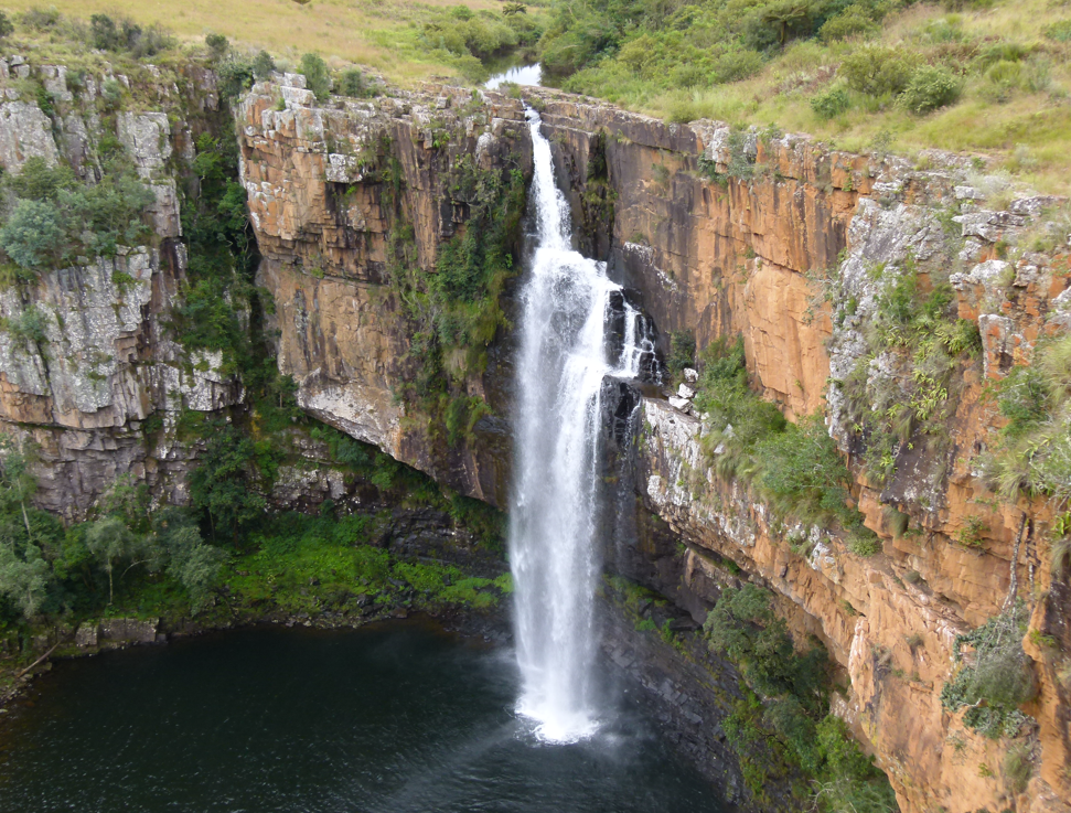 Een waterval die neerstort in een donkere poel, omgeven door rotswanden en groene vegetatie.