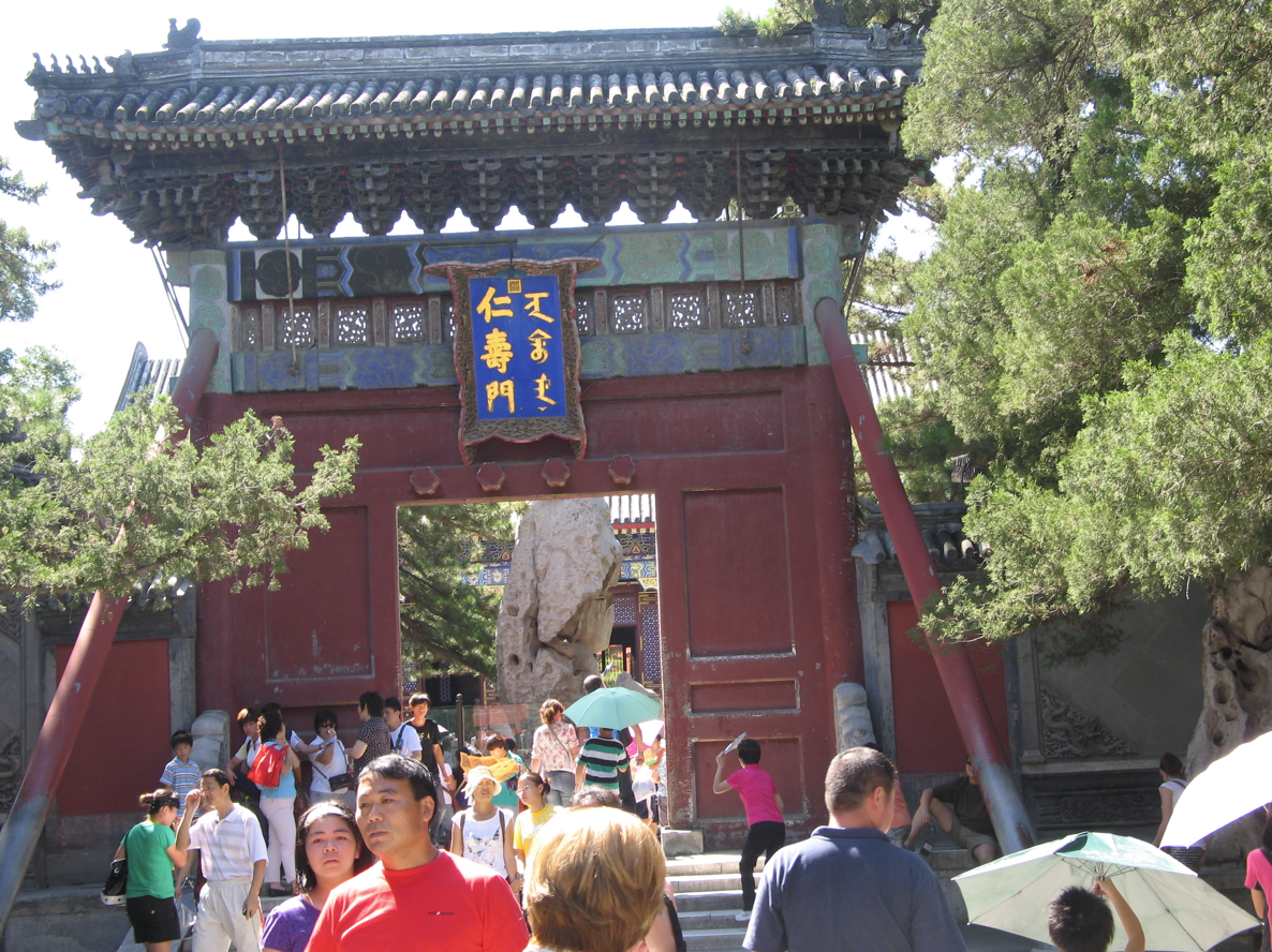 Een rood-blauwe Chinese poort met een menigte mensen die erdoorheen loopt.