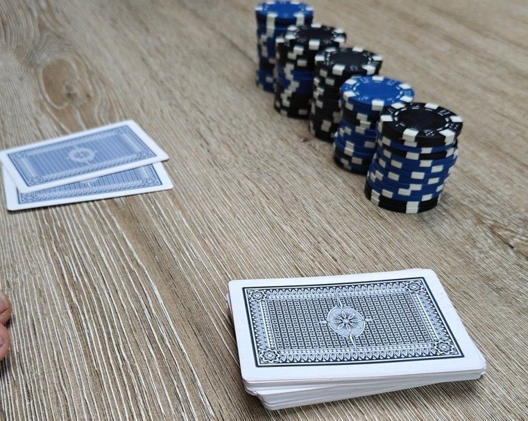 Een houten tafel met een pak speelkaarten, twee hole cards en verschillende stapels zwarte en blauwe pokerfiches.