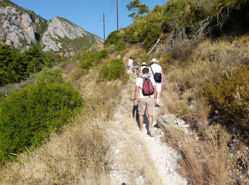 Wandelaars op een droog, onverhard pad met bergen en begroeiing op de achtergrond.