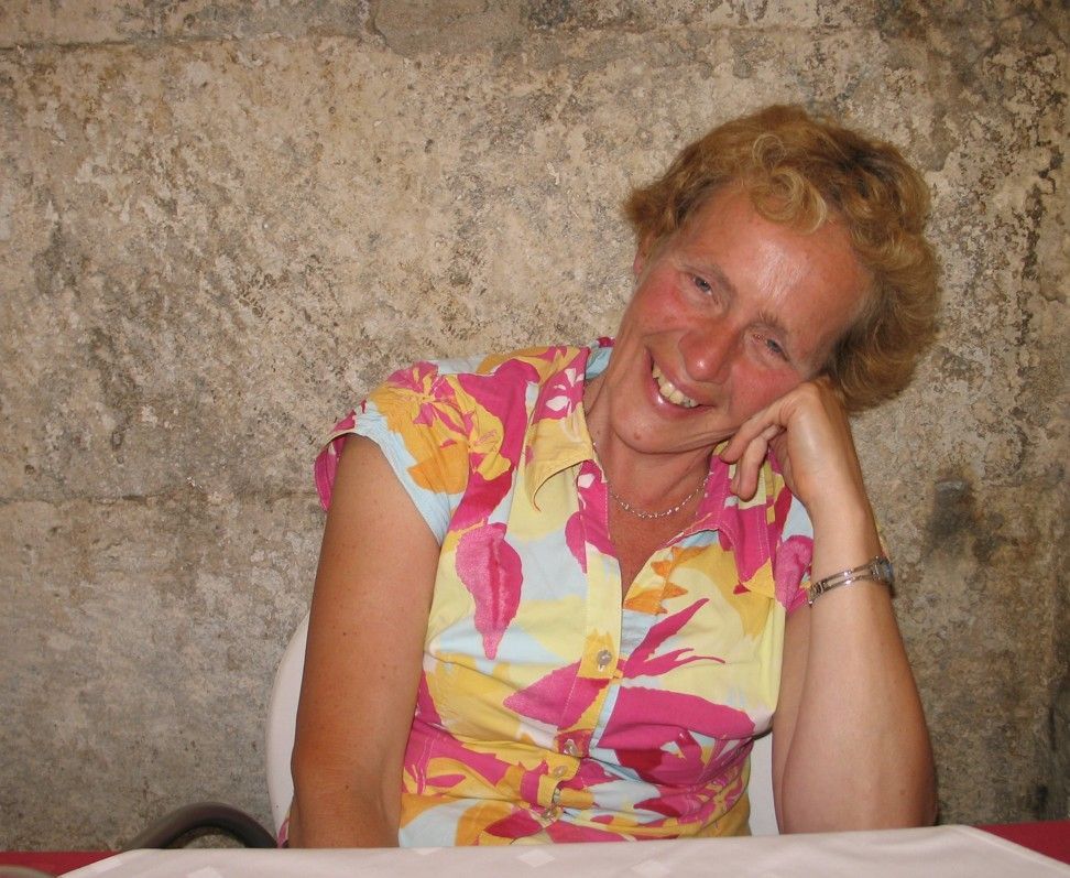 Een vrouw in een felgekleurde top met bloemenprint glimlacht en laat haar hoofd op haar hand rusten.