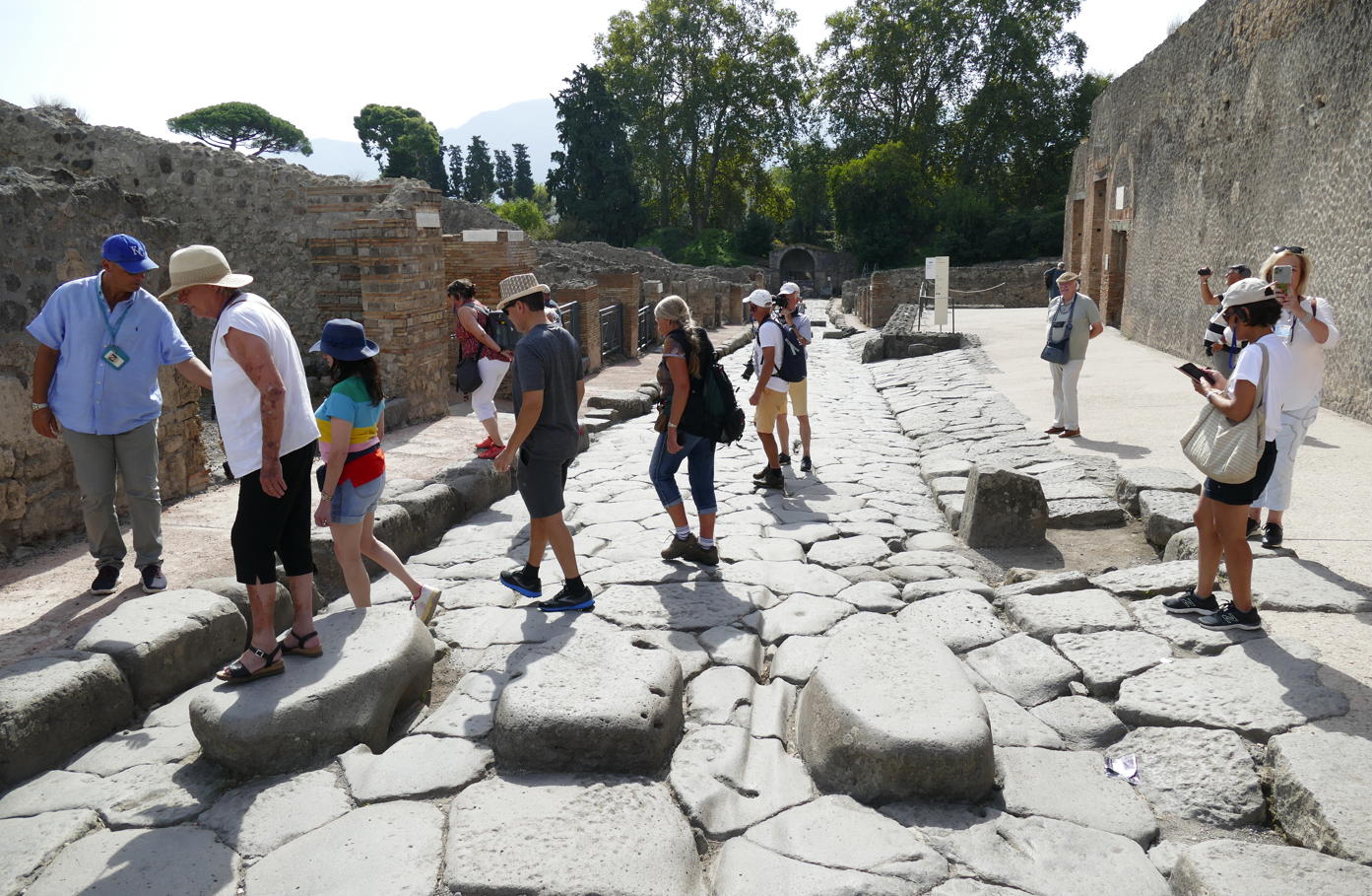 Mensen lopen over een stenen straat in Pompeii, Italië, tussen oude ruïnes; zonnige dag.