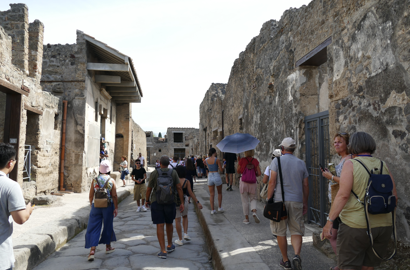 Mensen lopen door een smalle straat in Pompeii, langs verweerde stenen gebouwen.