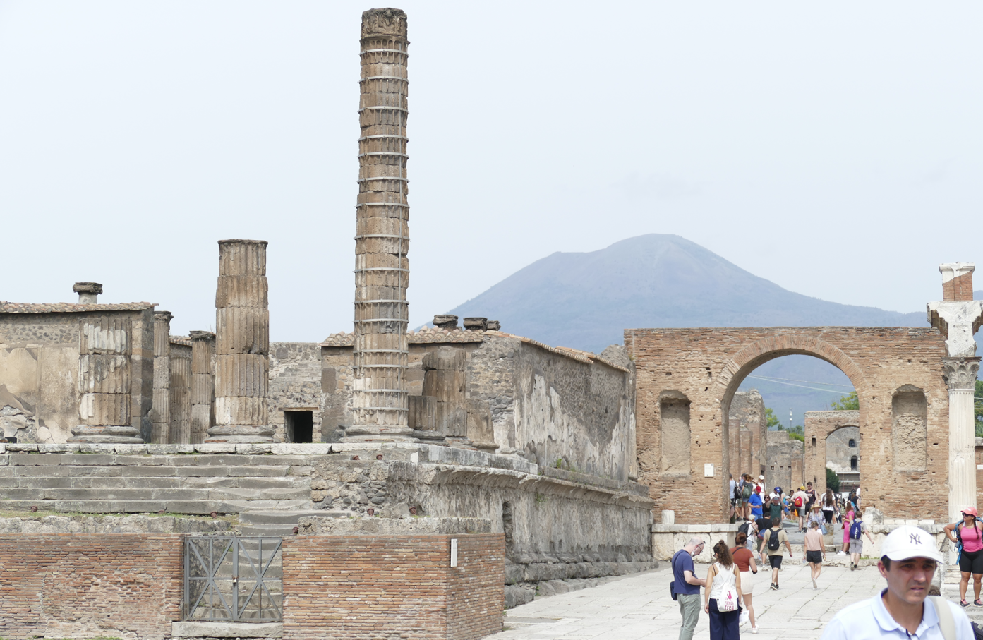 Oude ruïnes in Pompeii, Italië, met de Vesuvius op de achtergrond; toeristen lopen over een geplaveide straat.