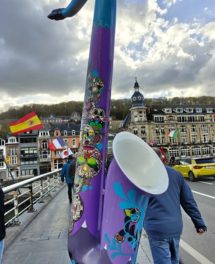 Een gigantische, paarse, met graffiti beschilderde saxofoonsculptuur op een brug in Dinant, België.