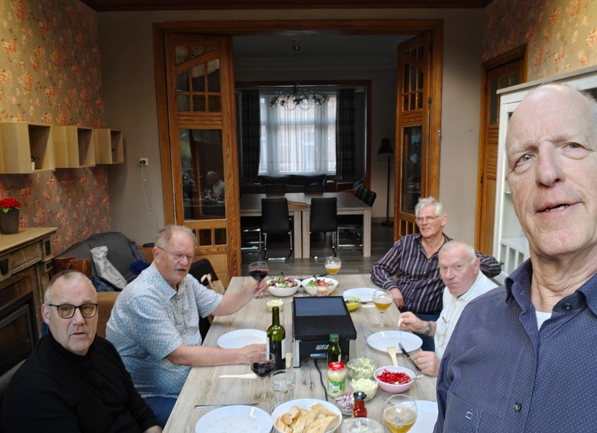 Vijf mensen zitten rond een houten eettafel en eten en drinken samen in een sfeervol verlichte, huiselijke eetkamer.