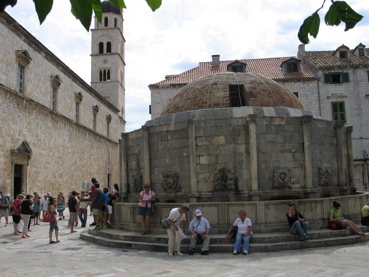 De Onofrio-fontein in Dubrovnik, Kroatië, een stenen constructie en een klokkentoren op de achtergrond.